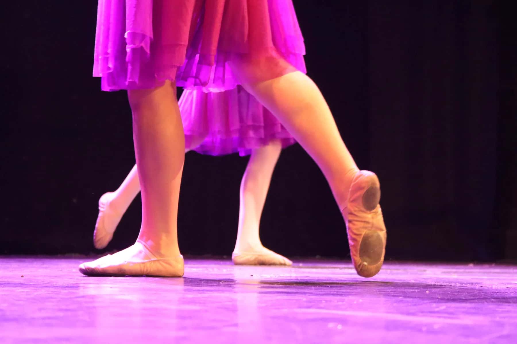 Ballet dancers' feet in pink ballet shoes beneath pink skirts on a lit stage