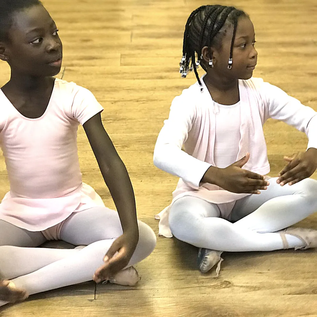 Two young ballet students sitting on the studio floor