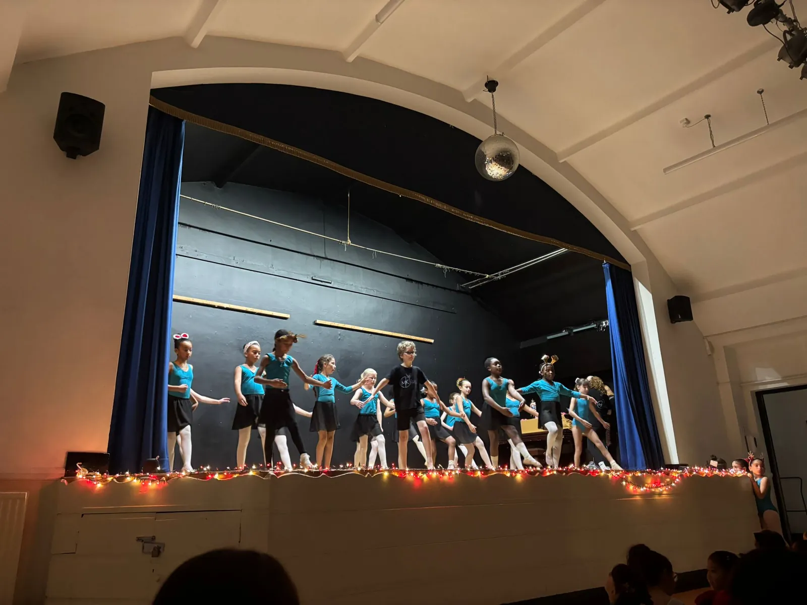Dancers performing on stage at the Christmas Showcase, with festive lights along the stage