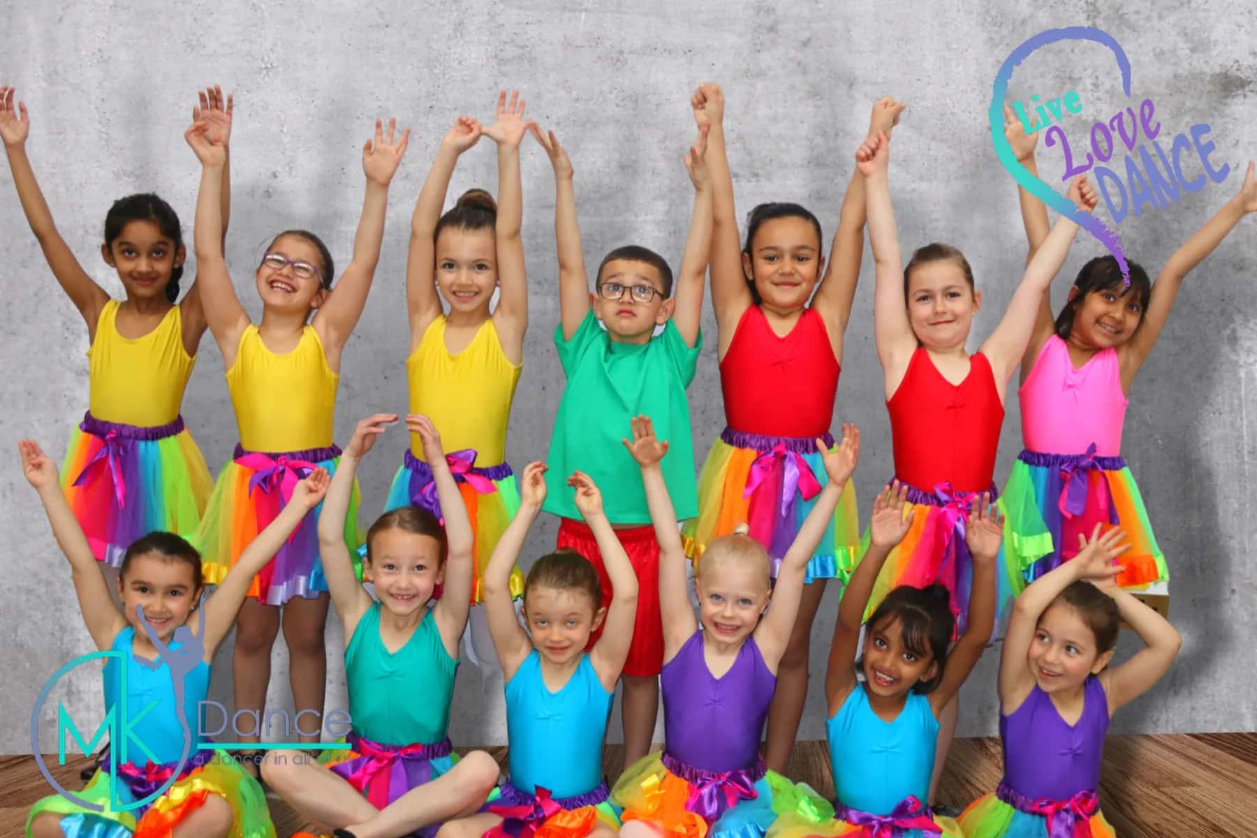 A group of children in colourful leotards posing with arms raised at a photo shoot