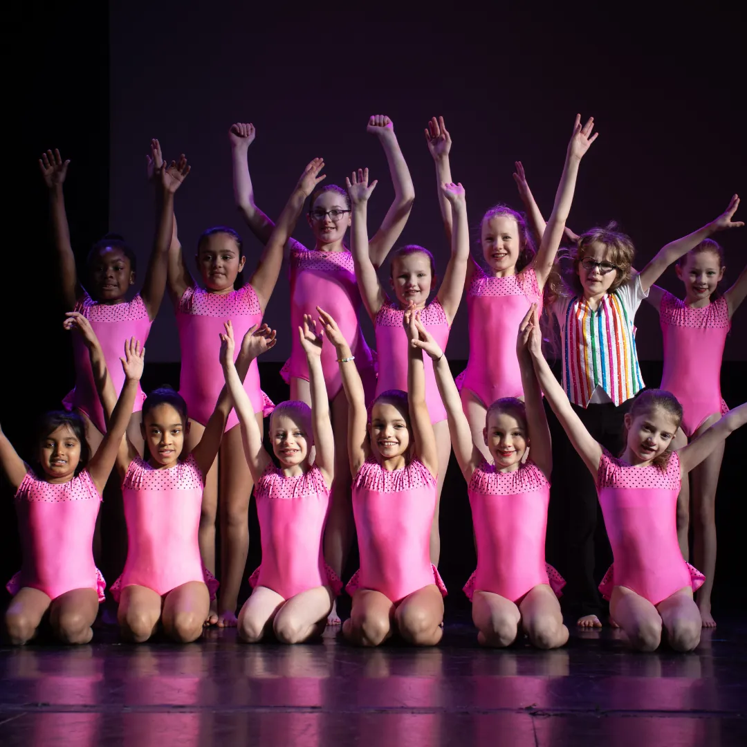 A group of young dancers in pink costumes posing on stage