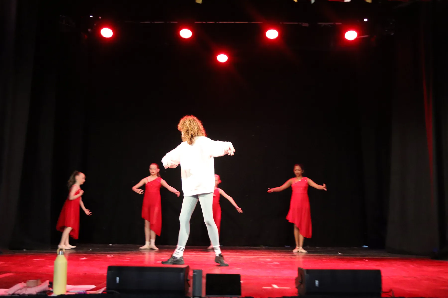 Dancers in red performing around a performer in white at an MK Dance show