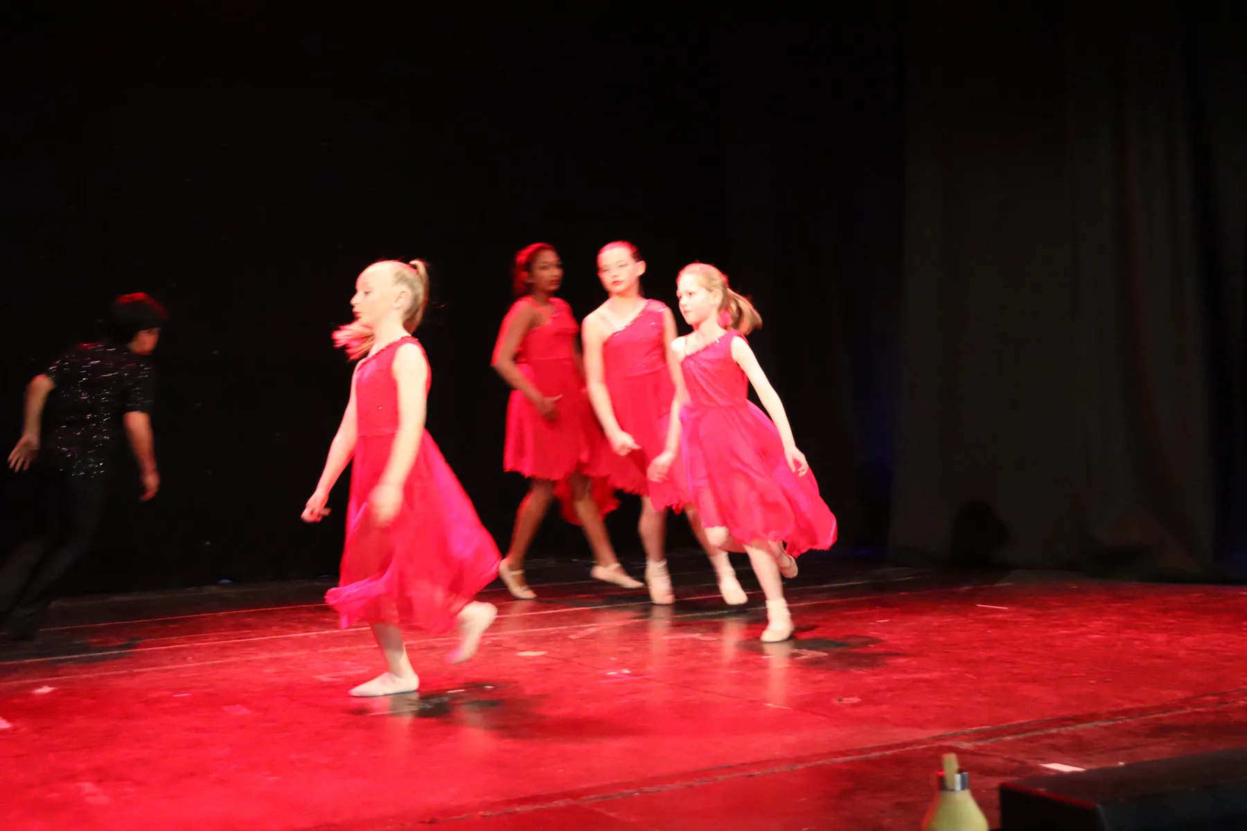 Young dancers in red dresses performing on a red-lit stage