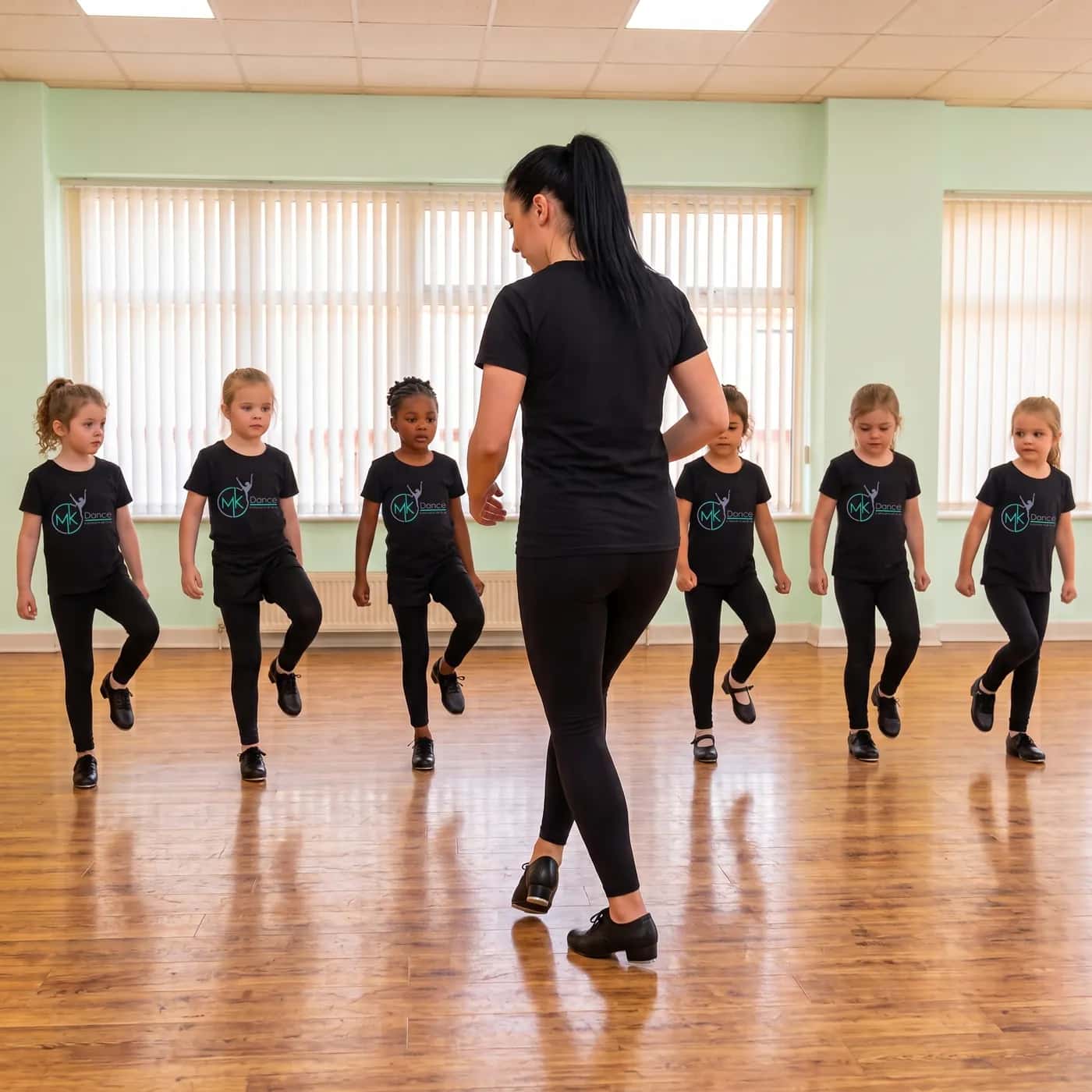 A teacher leading a tap class of children dressed in black in a bright studio