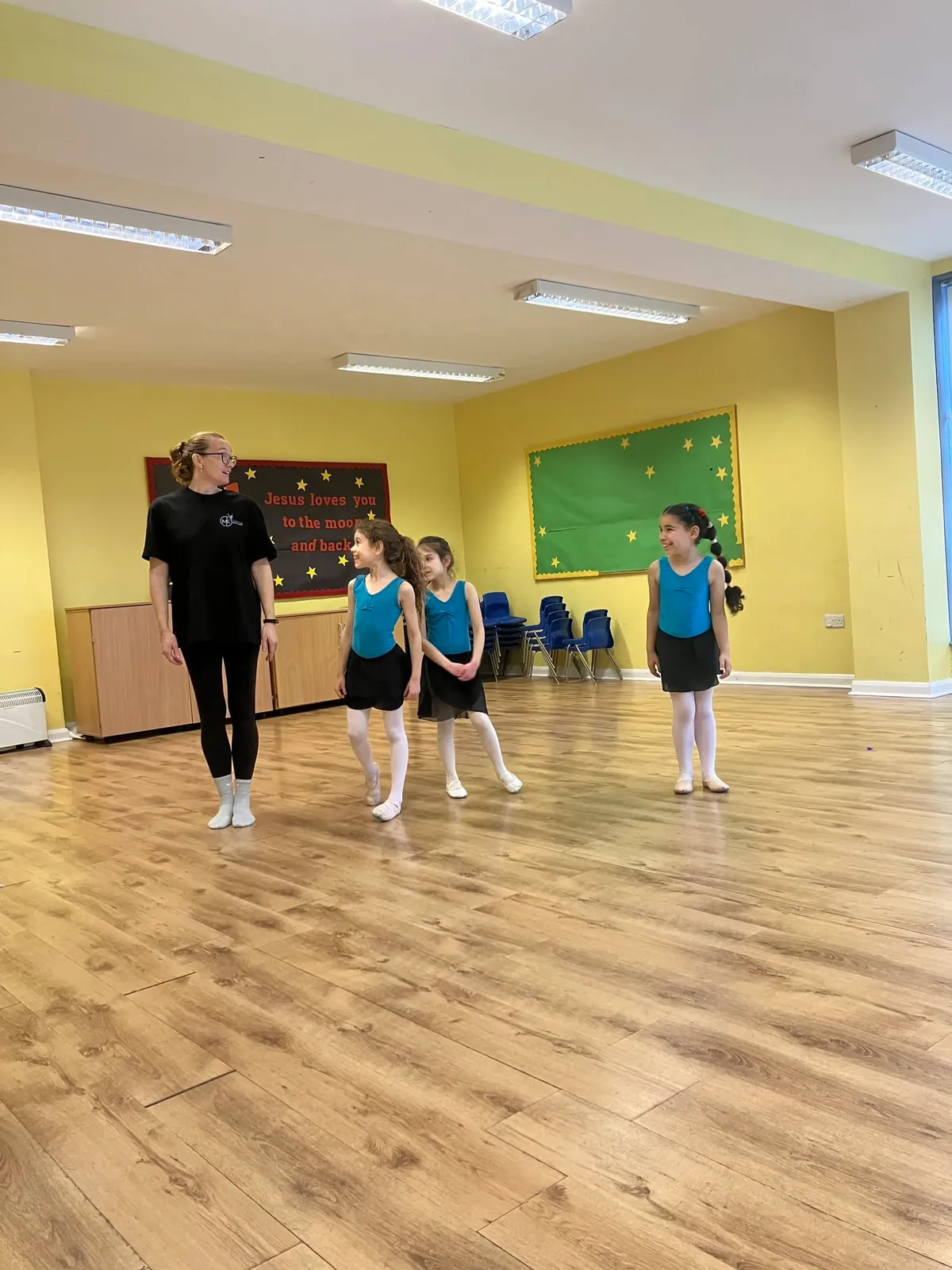 A teacher leading a class of young children in turquoise leotards